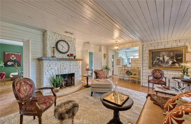 living area with wood finished floors, wood ceiling, a stone fireplace, and wooden walls