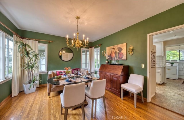 dining space featuring washer / dryer, a chandelier, light wood-type flooring, and baseboards