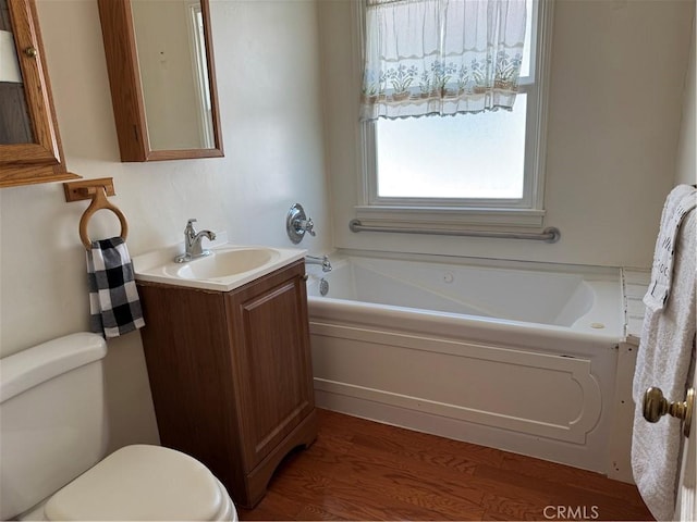 full bath featuring toilet, a garden tub, wood finished floors, and vanity