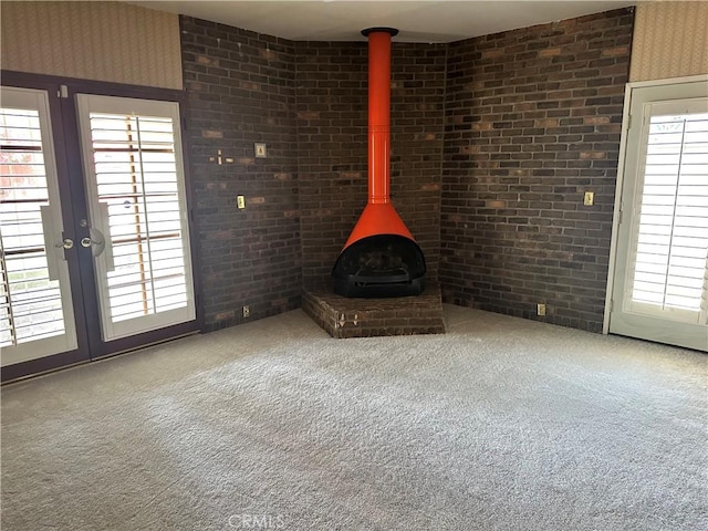 unfurnished living room with a wood stove, carpet floors, plenty of natural light, and brick wall