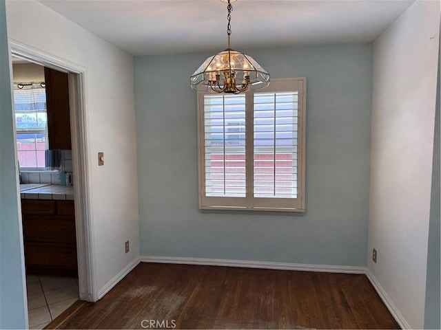 unfurnished dining area featuring a chandelier, wood finished floors, and baseboards