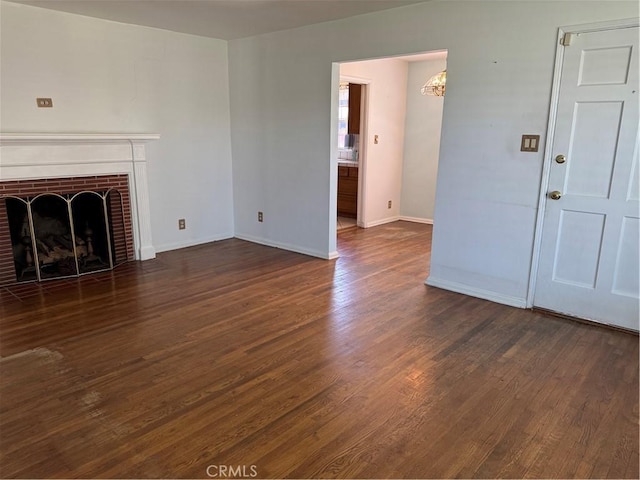 unfurnished living room featuring wood finished floors, baseboards, a brick fireplace, and a chandelier