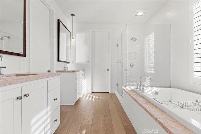 full bath featuring a stall shower, wood finished floors, a garden tub, and two vanities