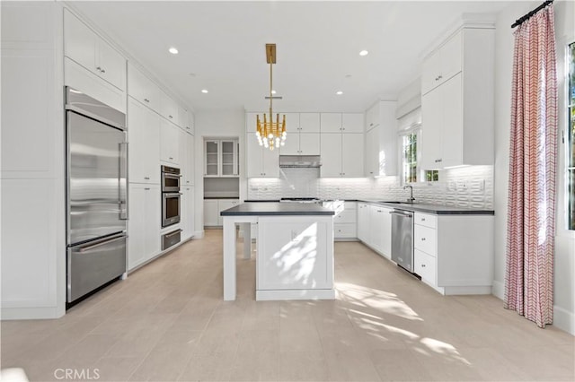 kitchen with appliances with stainless steel finishes, a warming drawer, dark countertops, a chandelier, and a kitchen island