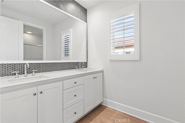 full bath featuring decorative backsplash, baseboards, wood finished floors, double vanity, and a shower with shower door