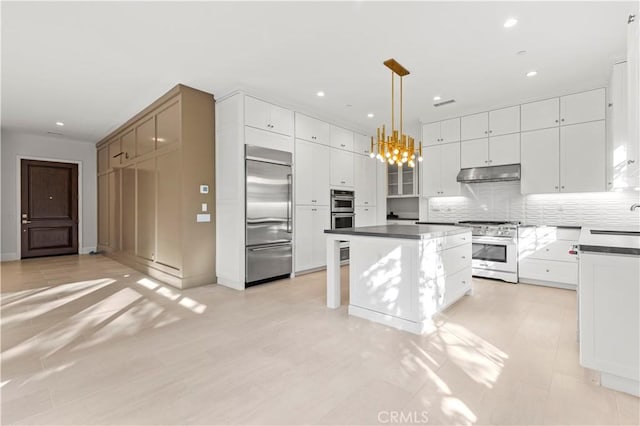 kitchen with high quality appliances, dark countertops, under cabinet range hood, a kitchen island, and recessed lighting