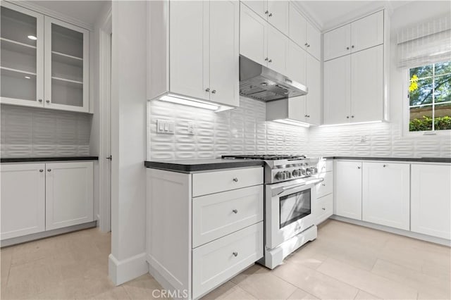kitchen featuring high end range, under cabinet range hood, dark countertops, tasteful backsplash, and white cabinetry