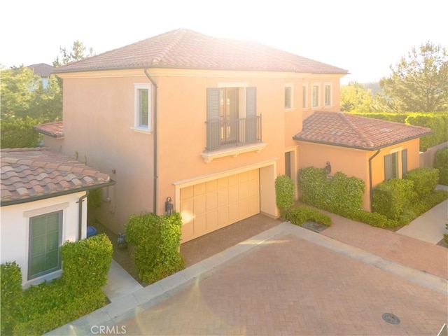 view of front of property featuring a balcony, stucco siding, decorative driveway, an attached garage, and a tile roof
