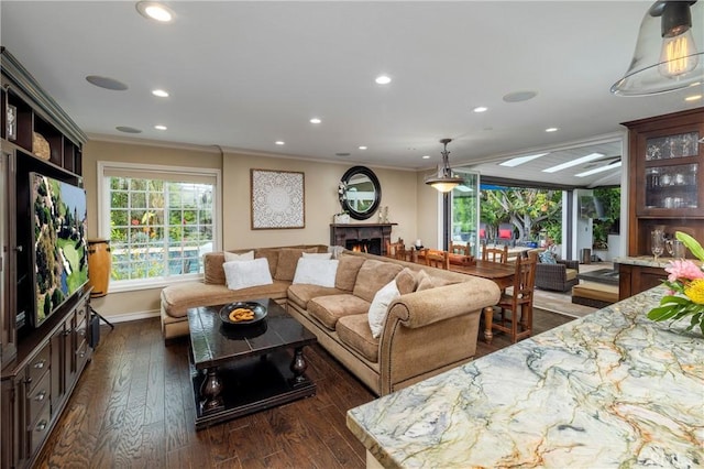 living area featuring crown molding, dark wood-style flooring, recessed lighting, a warm lit fireplace, and baseboards