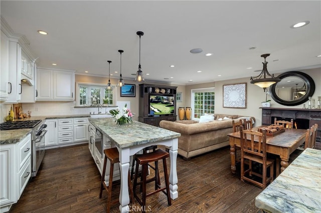 kitchen featuring high end stove, open floor plan, white cabinetry, light stone counters, and recessed lighting
