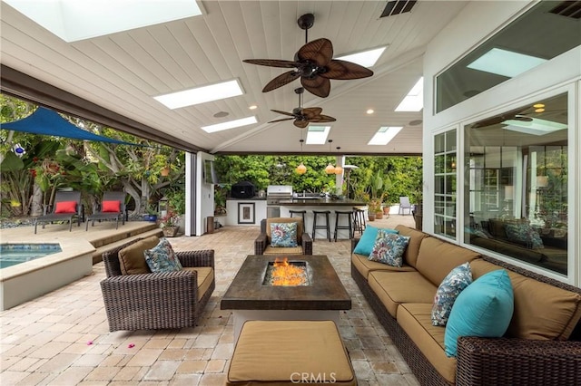 view of patio / terrace featuring an outdoor living space with a fire pit, exterior bar, area for grilling, and ceiling fan