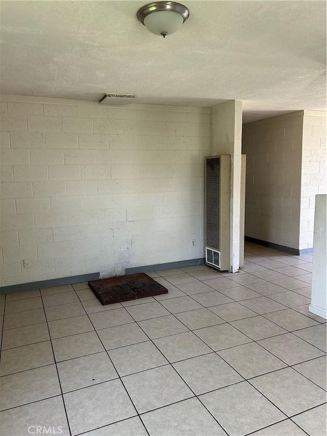 empty room featuring a heating unit, concrete block wall, a textured ceiling, and light tile patterned flooring