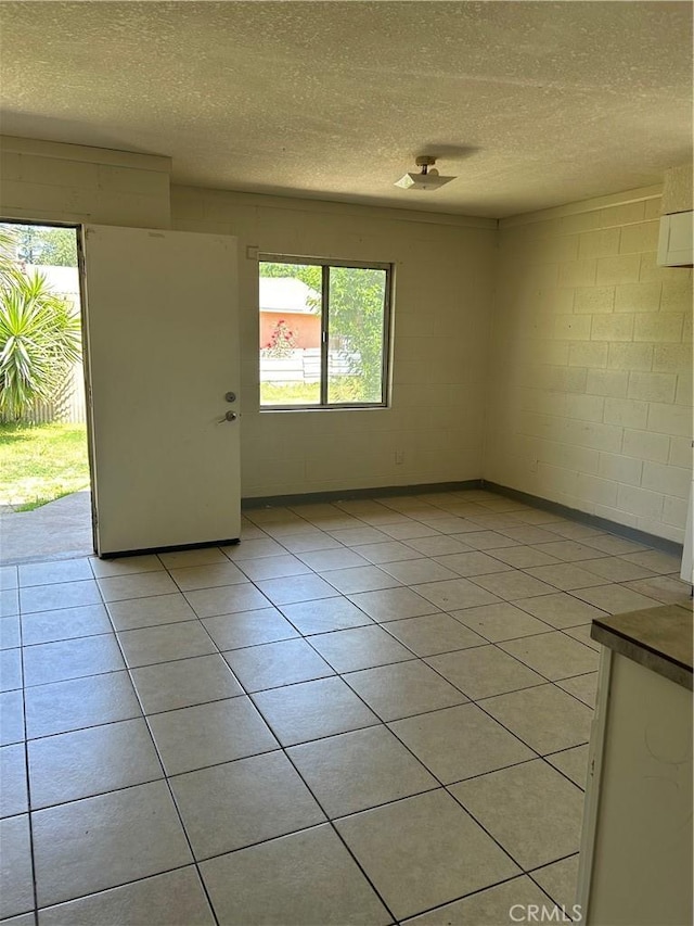 spare room featuring a textured ceiling, concrete block wall, healthy amount of natural light, and light tile patterned flooring