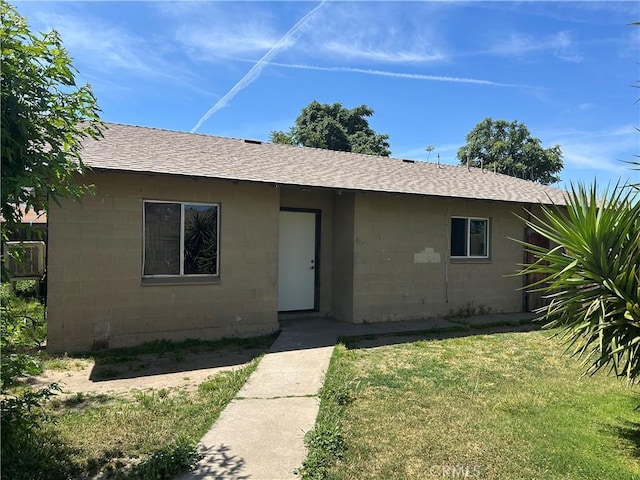 single story home with concrete block siding, a shingled roof, and a front lawn