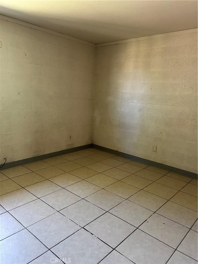 spare room featuring light tile patterned floors and concrete block wall