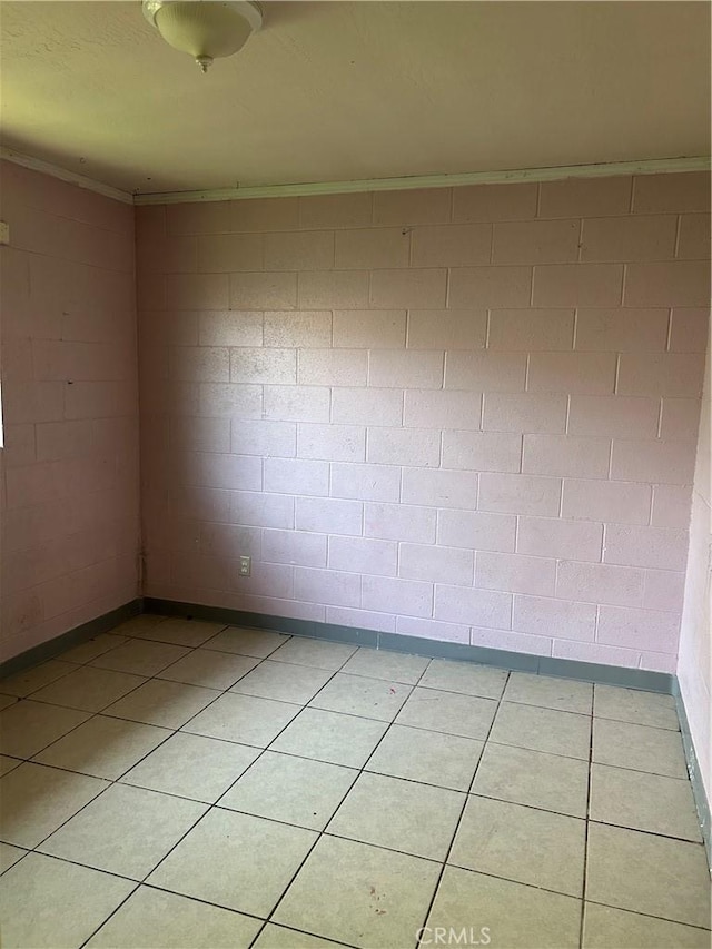 spare room with concrete block wall, crown molding, and light tile patterned floors