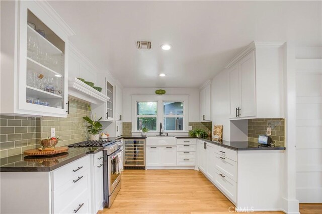 kitchen with stainless steel range, beverage cooler, a sink, dark countertops, and backsplash