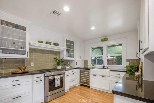 kitchen with wine cooler, stainless steel gas range, a sink, white cabinetry, and recessed lighting