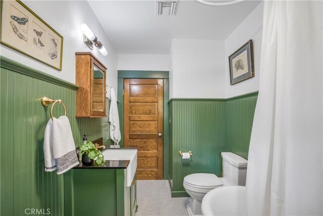 bathroom with toilet, vanity, wainscoting, and tile patterned flooring