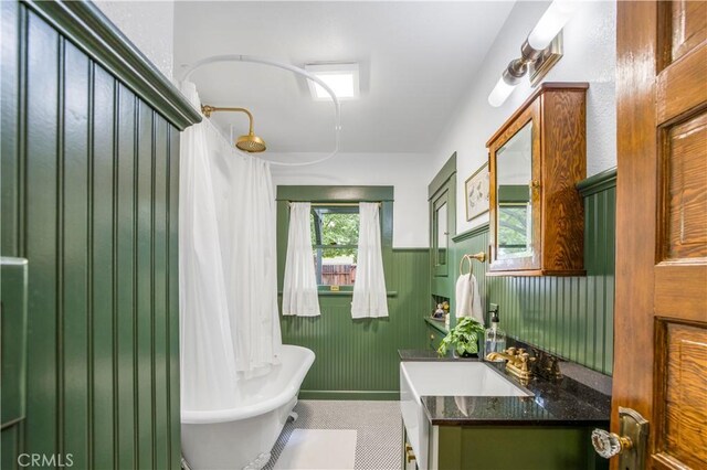 full bathroom featuring a soaking tub, a wainscoted wall, and vanity