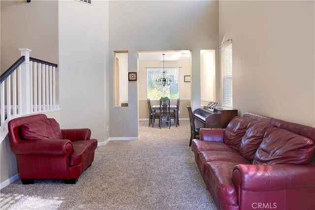 living area featuring a chandelier, carpet flooring, a high ceiling, and baseboards