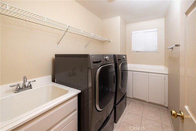 laundry area featuring washing machine and dryer, cabinet space, and light tile patterned floors