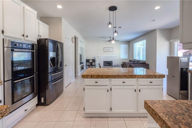 kitchen featuring black refrigerator with ice dispenser, double oven, ceiling fan, a tile fireplace, and light tile patterned flooring