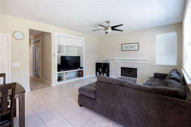 living area with built in features, a ceiling fan, light tile patterned floors, a fireplace, and baseboards