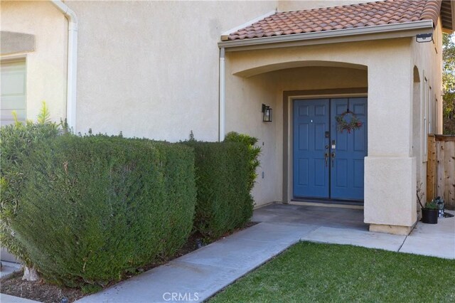 doorway to property featuring stucco siding, a tiled roof, and fence