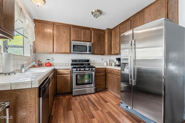 kitchen with appliances with stainless steel finishes, tile countertops, a sink, and dark wood-type flooring