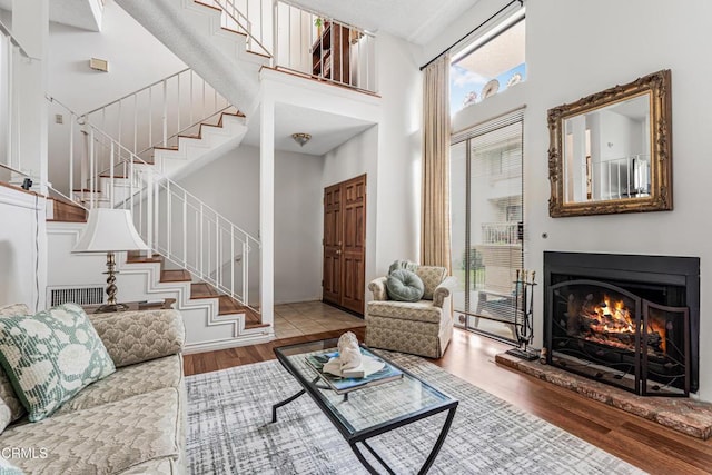 living room featuring wood finished floors, a high ceiling, stairs, a warm lit fireplace, and baseboards