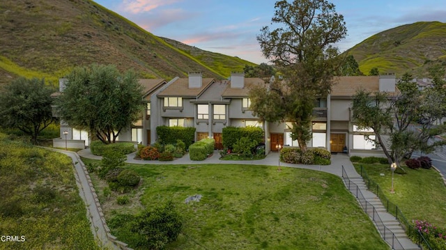 view of front facade with stucco siding, a chimney, a mountain view, and a front yard