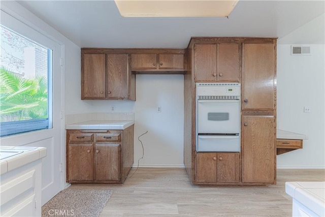 2726 W Orion Ave, Santa Ana, CA 92704 - kitchen featuring oven, a warming drawer, brown cabinets, tile counters, and light wood-style floors