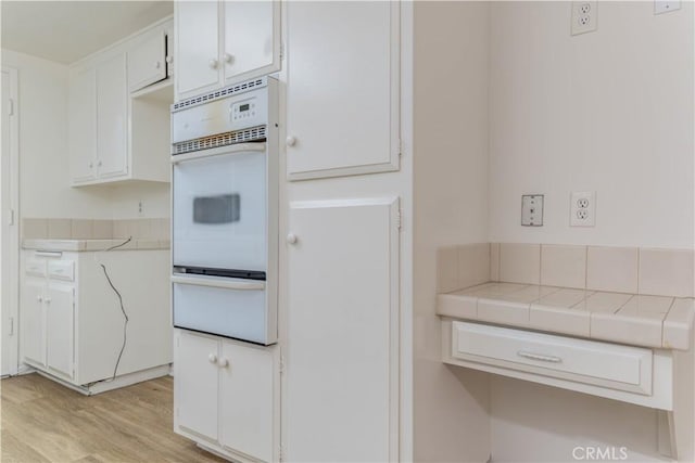 2726 W Orion Ave, Santa Ana, CA 92704 - kitchen with a warming drawer, white oven, white cabinets, light wood-style floors, and tile countertops