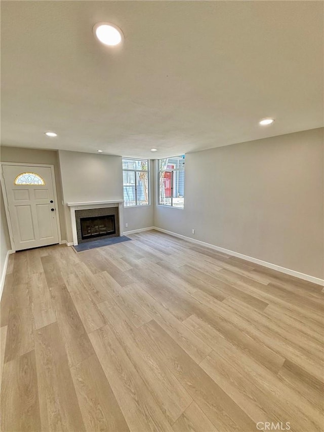 unfurnished living room featuring baseboards, recessed lighting, light wood-style floors, and a fireplace with flush hearth