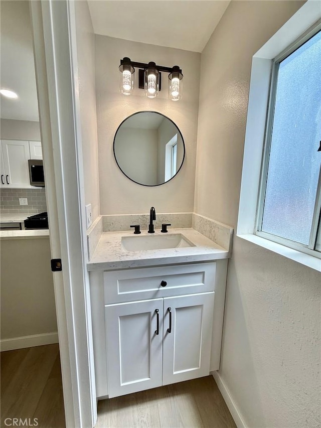 bathroom featuring wood finished floors, vanity, decorative backsplash, and baseboards