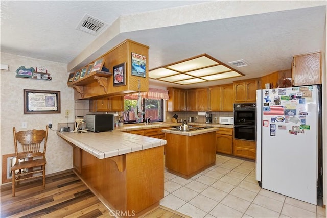20407 Eyota Ln, Apple Valley, CA 92308 - kitchen featuring stainless steel appliances, tile countertops, a peninsula, brown cabinets, and a center island