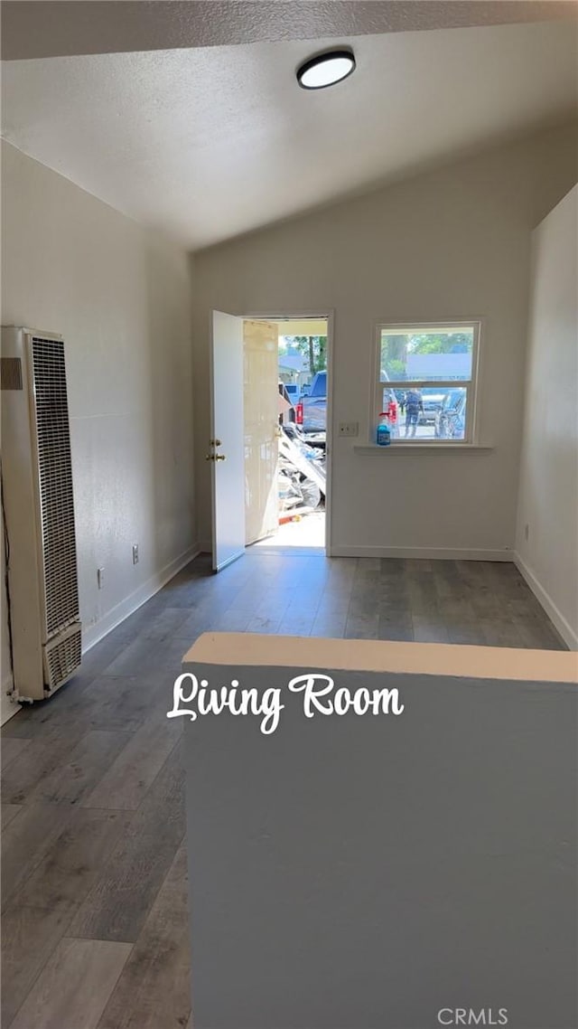 spare room with a heating unit, vaulted ceiling, wood finished floors, a textured ceiling, and baseboards