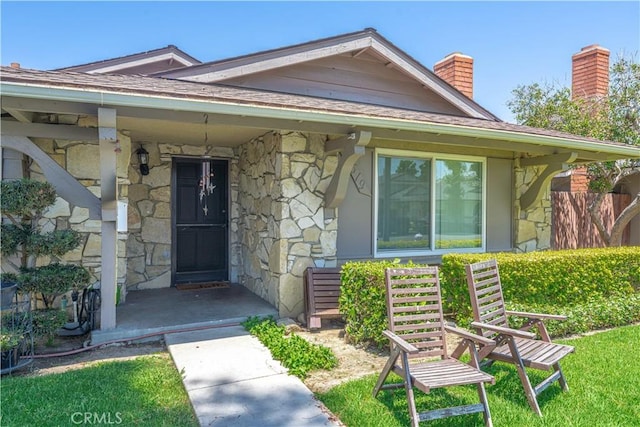 2619 W Aurora St, Santa Ana, CA 92704 - doorway to property featuring stone siding, a chimney, covered porch, and roof with shingles