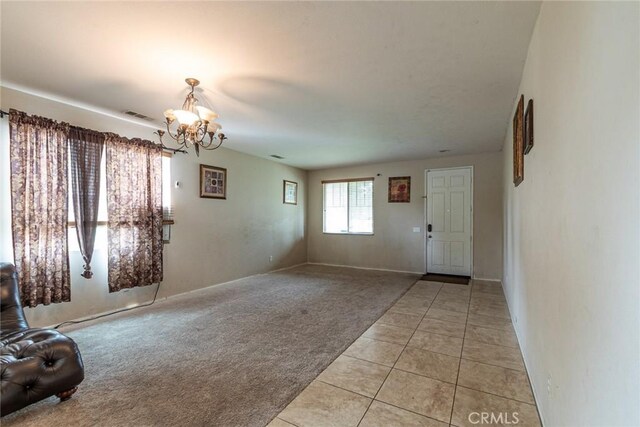 entryway with a chandelier, light tile patterned floors, light colored carpet, and baseboards