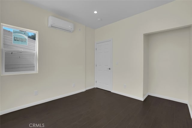 unfurnished room with an AC wall unit, dark wood-style flooring, baseboards, and recessed lighting