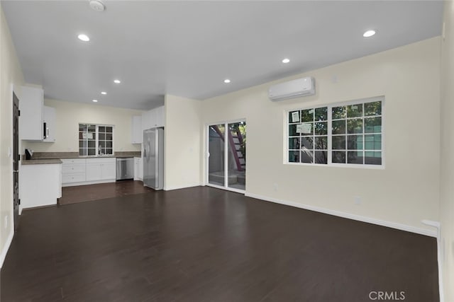 unfurnished living room with a wall unit AC, recessed lighting, dark wood-style floors, baseboards, and a sink