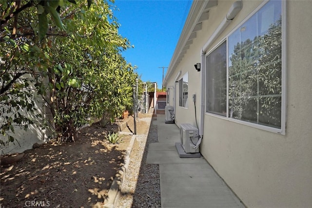 view of side of property featuring stucco siding, a cooling unit, a patio area, and fence
