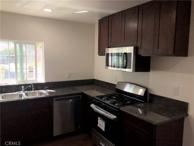 kitchen with stainless steel appliances, dark countertops, dark brown cabinetry, a sink, and recessed lighting