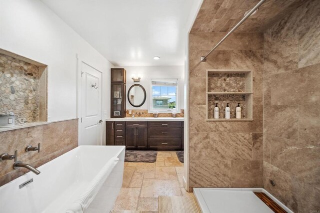 full bath with vanity, a tile shower, a freestanding bath, stone tile floors, and tile walls