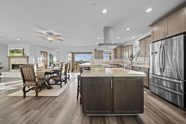 kitchen featuring freestanding refrigerator, island range hood, a kitchen bar, a ceiling fan, and recessed lighting