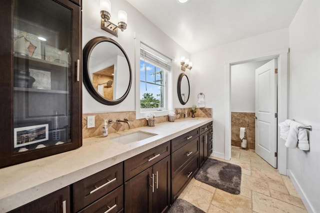 full bathroom with stone tile floors, double vanity, and baseboards