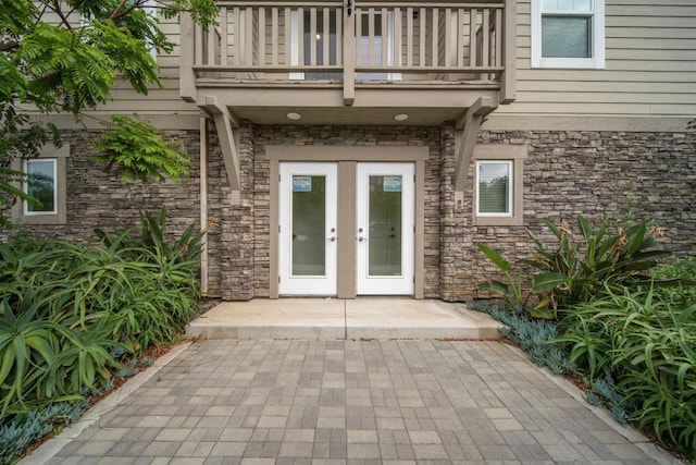 property entrance with a balcony, stone siding, and french doors