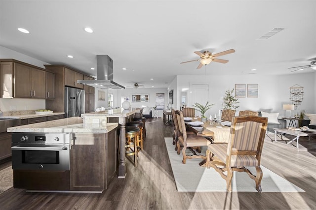 kitchen with island exhaust hood, appliances with stainless steel finishes, a ceiling fan, open floor plan, and recessed lighting