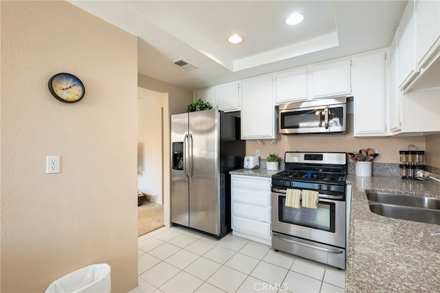 kitchen with stainless steel appliances, a sink, light tile patterned floors, white cabinets, and a textured wall